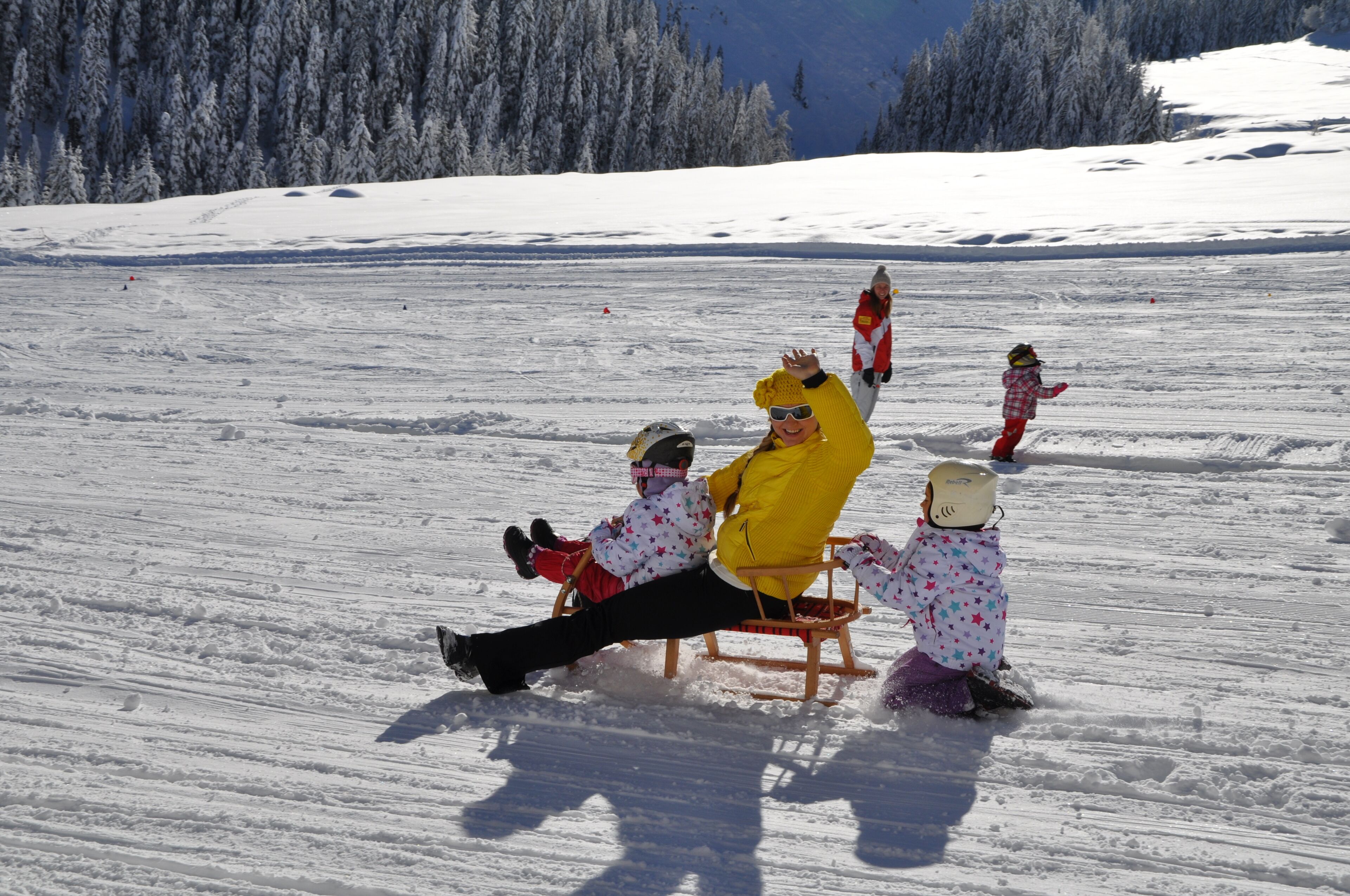 A snowy landscape with a person sitting on a sled, accompanied by two children.