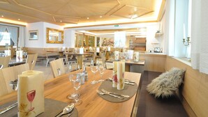 A dining area with wooden tables, chairs, and a fur throw on one table. - Hotel Traube – Stelvio (Stelvio)