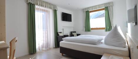 Un dormitorio con cama, escritorio, silla, televisor y ventana con cortinas.