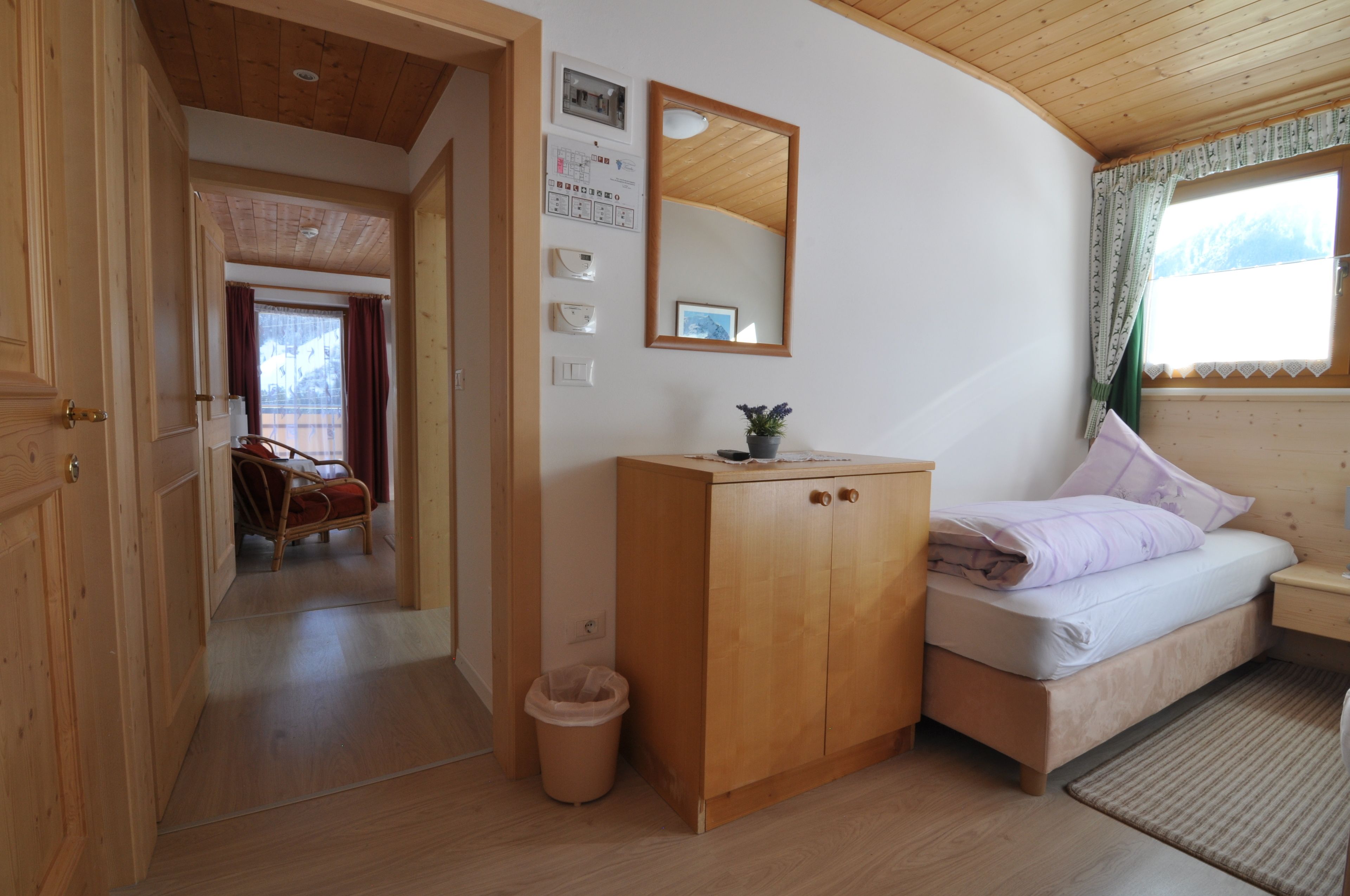 A wooden-paneled room with a bed, a wooden cabinet, a mirror, and a window with curtains.