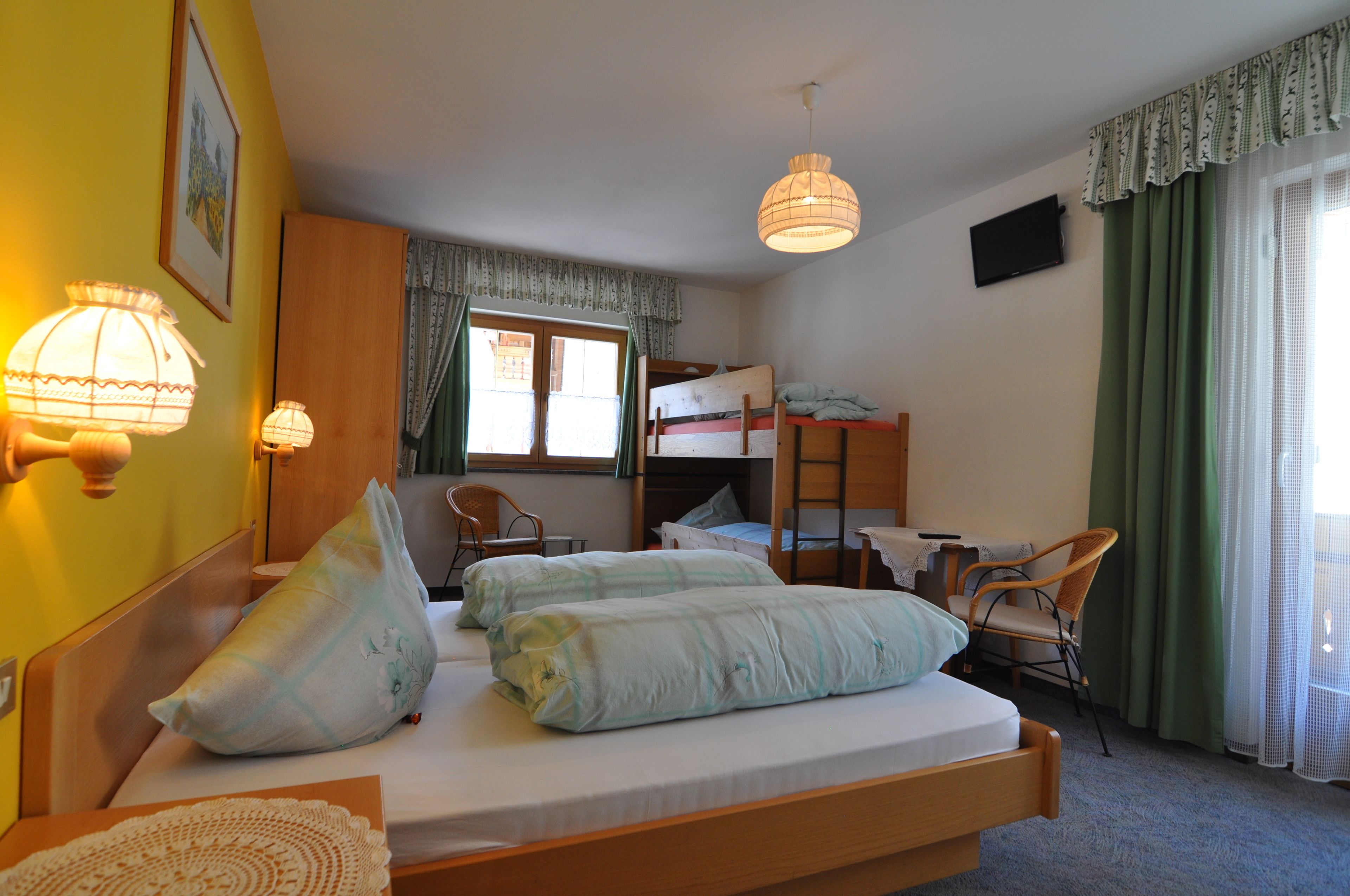 A room with a bed, two chairs, a desk, a bunk bed, and a television.