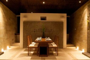 A dining area with a wooden table set for four, surrounded by chairs, in a room with stone walls and a wooden ceiling.