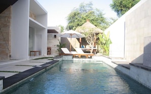 A pool area with lounge chairs and a thatched-roof structure.