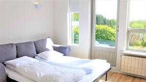 A neatly made bed in a room with large windows, a radiator, and a light fixture on the wall. -  Veghús Guesthouse (Selfoss)