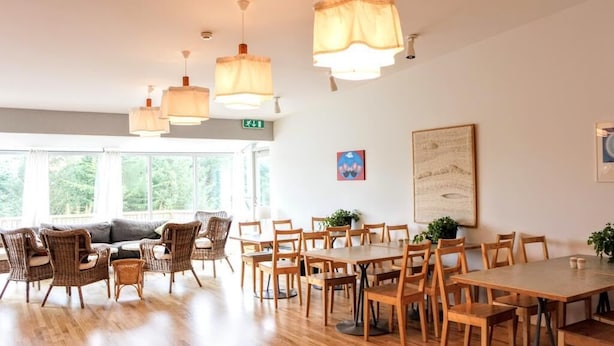A dining area with wooden tables and chairs, hanging pendant lights, and a sofa in the background. -  Veghús Guesthouse (Selfoss)