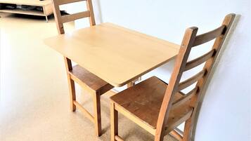 Una mesa de comedor de madera con cuatro sillas, un estante de madera pequeño y un control remoto sobre la mesa.