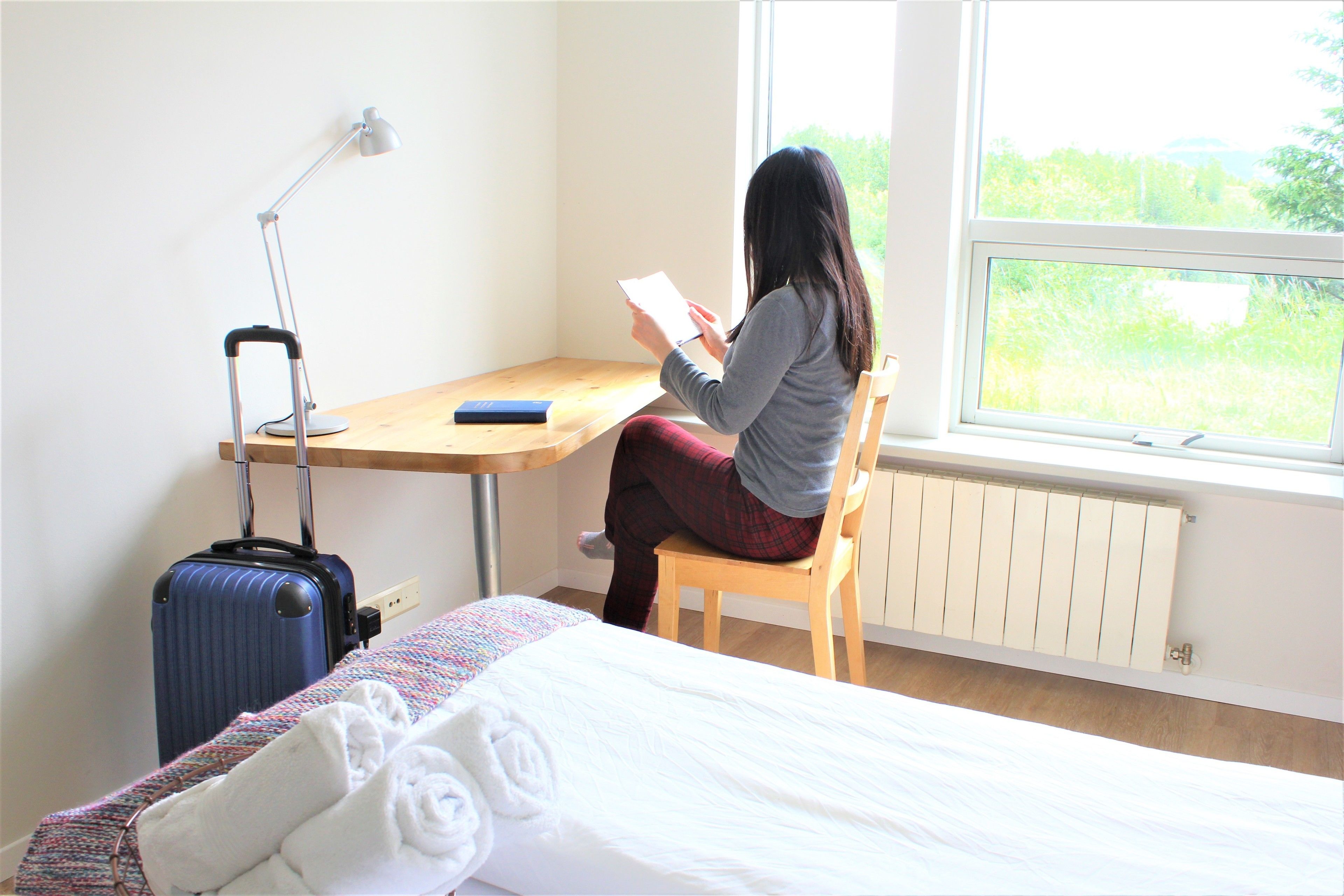 A room with a bed, a desk, a chair, a window, and a suitcase.