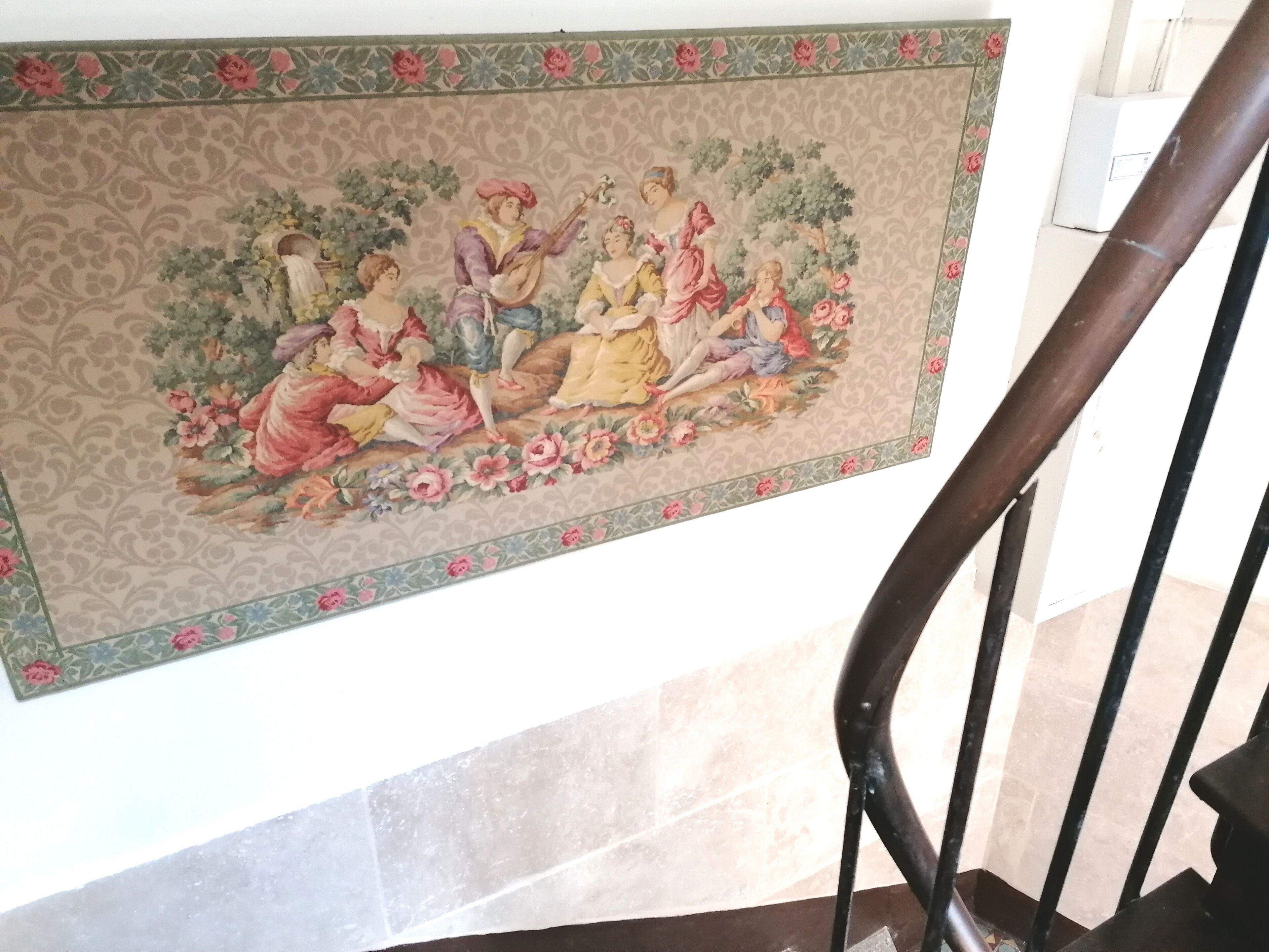 A mural with a pastoral scene, a staircase with black railings, and a tiled floor.