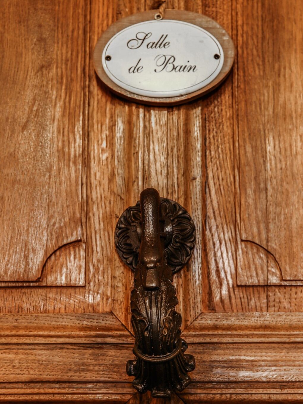Una puerta de madera con una placa de metal que dice 'Salle de Bain' y un llamador de aldaba decorativo.