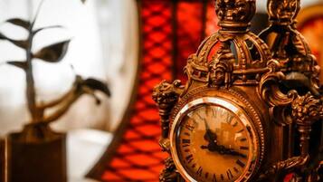 An ornate clock with Roman numerals, set against a blurred background with a red patterned wall.