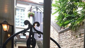 A view through a window of a courtyard with a stone wall, a wooden door, a metal staircase, and a hanging light fixture. - Le Petit Tertre (Dijon)