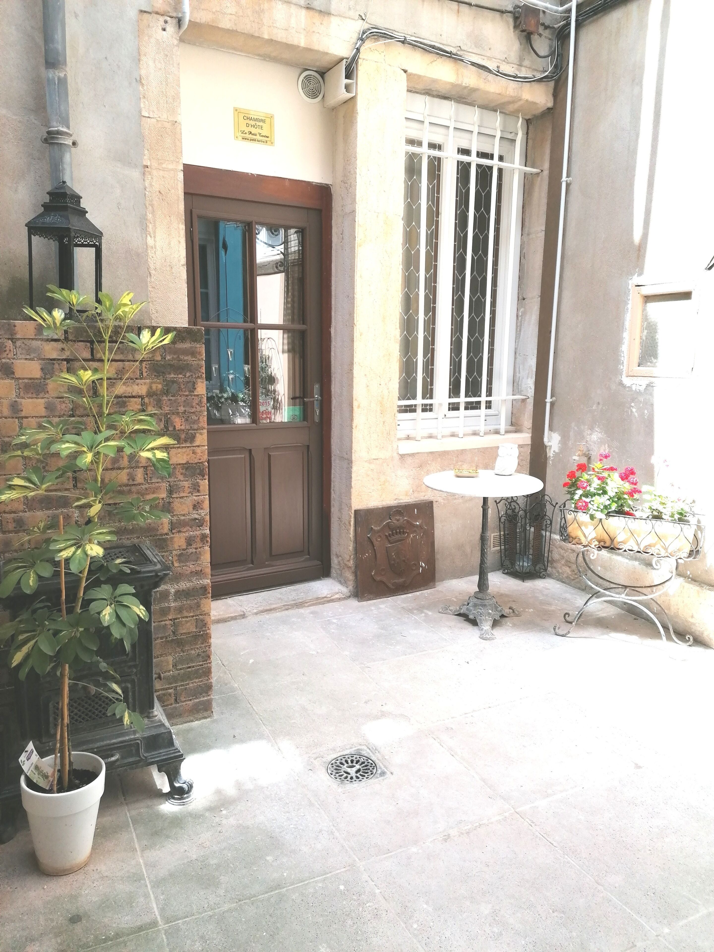 A building entrance with a brown door, a window with metal bars, a potted plant, a small table, and a flower pot.
