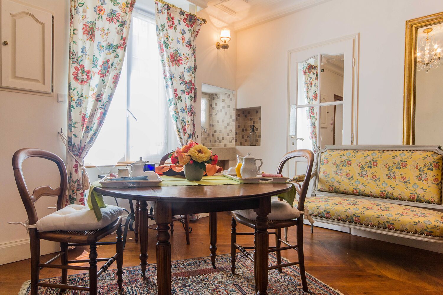 Un comedor con una mesa redonda, cortinas con motivos florales y un sofá floral.
