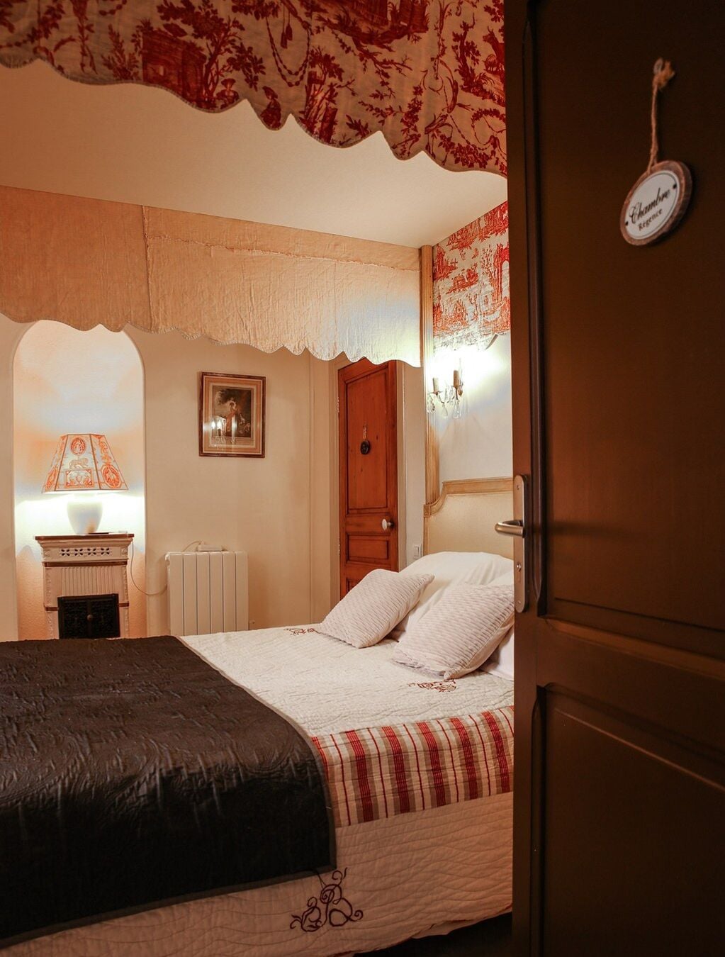 Un dormitorio con cama, radiador, lámpara y puerta con un cartel.
