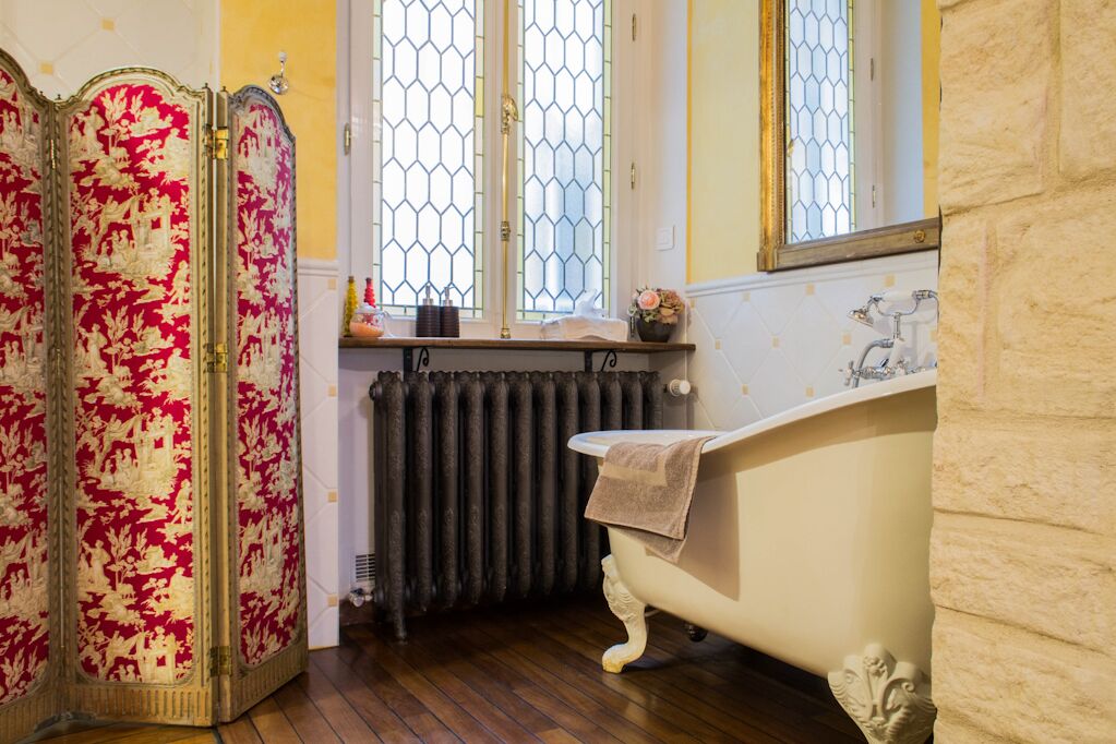 Une salle de bain dotée d’une baignoire sur pieds d’époque, d’un radiateur et d’une fenêtre ornée de motifs décoratifs en verre.