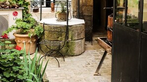A stone courtyard with a metal table, potted plants, and a black door. - Le Petit Tertre (Dijon)