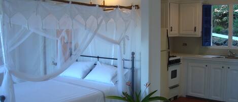 Une chambre à coucher avec un lit à baldaquin, une petite table avec une plante, et une cuisine avec des meubles blancs et une fenêtre.
