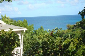 Vista costeira com um gazebo branco, vegetação exuberante e o oceano ao fundo.