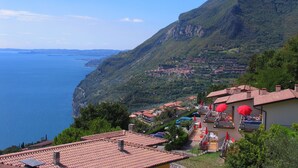 A coastal town with terracotta-roofed buildings, a view of the sea, and a hillside with scattered houses. - Hotel Residence La Rotonda (Tignale)