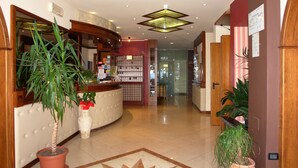 A hotel reception area with a curved counter, a potted plant, a bulletin board, and a tiled floor. - Hotel Residence La Rotonda (Tignale)
