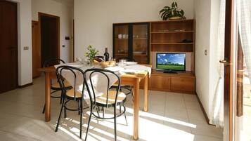 A dining area with a wooden table and chairs, a television, and a bookshelf.
