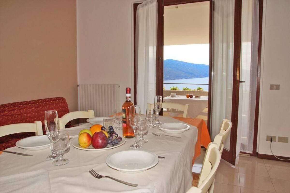 A dining table set with plates, cutlery, and fruit, with a view of mountains and water through an open door.