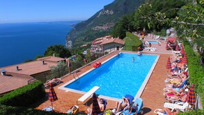 A pool area with a view of the sea, surrounded by greenery and buildings. - Hotel Residence La Rotonda (Tignale)