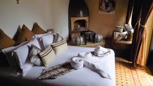 A neatly made bed with multiple pillows and a blanket, a small table with a vase, and a chair with a cushion. - Riad Belle Essaouira (Essaouira)
