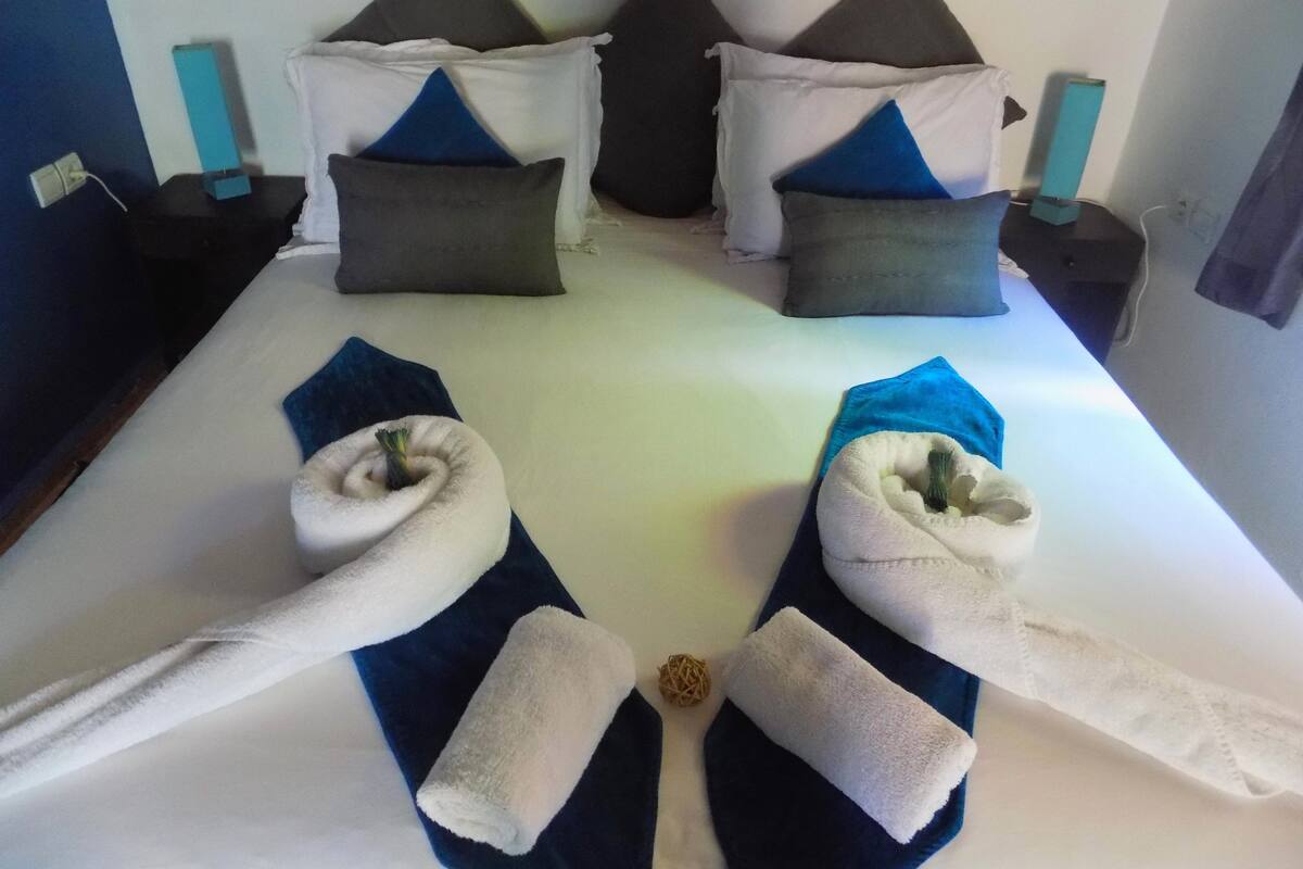 A neatly made bed with pillows, a blue blanket, and towels arranged on the bed.