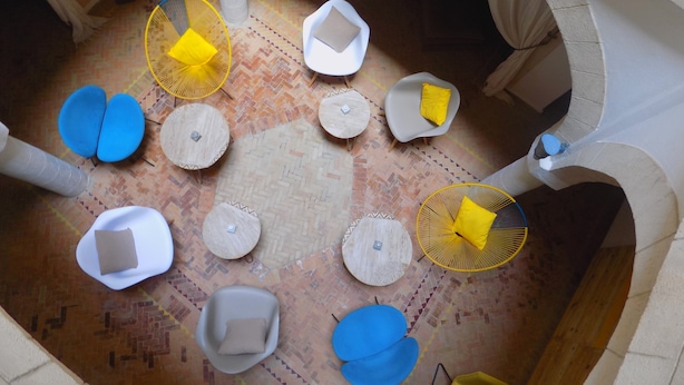 A circular seating area with various chairs and tables, a patterned floor, and a stone wall. - Riad Belle Essaouira (Essaouira)