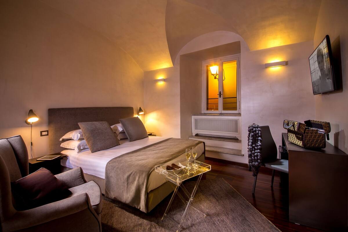 Una habitación de hotel con una cama, lámparas de noche, un escritorio y una silla.
