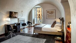 A modern bedroom with a bed, desk, and chairs, featuring an arched ceiling and a view of the city. - Palazzo De Cupis (Rome)