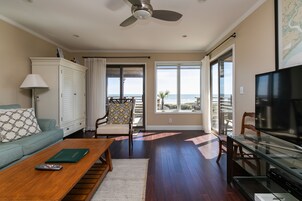 Sala de estar com sofá, mesa de centro, televisão e vista para o oceano através de grandes janelas.
