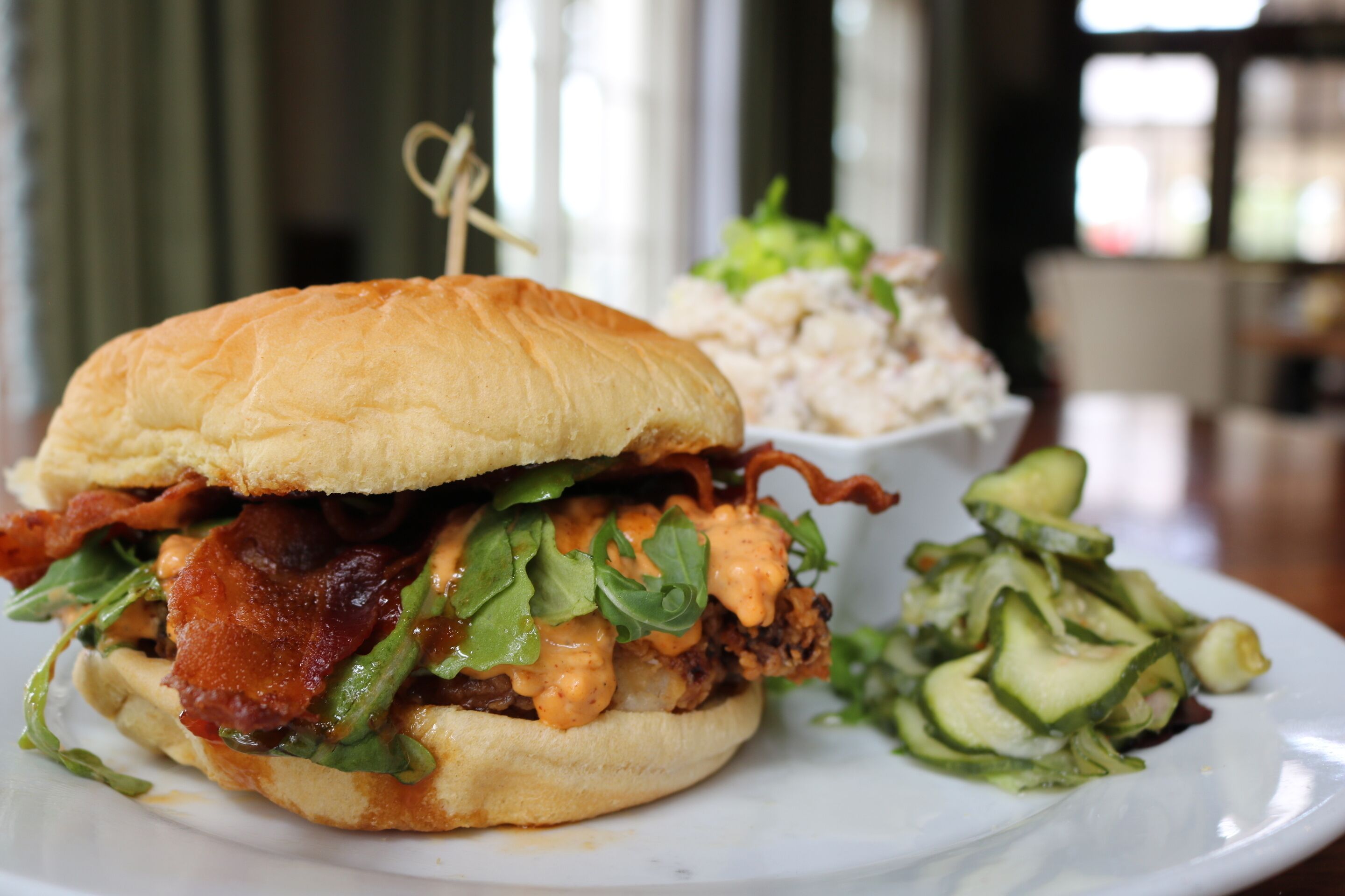 A sandwich with bacon, lettuce, and a creamy sauce, served with a side salad and a bowl of coleslaw.