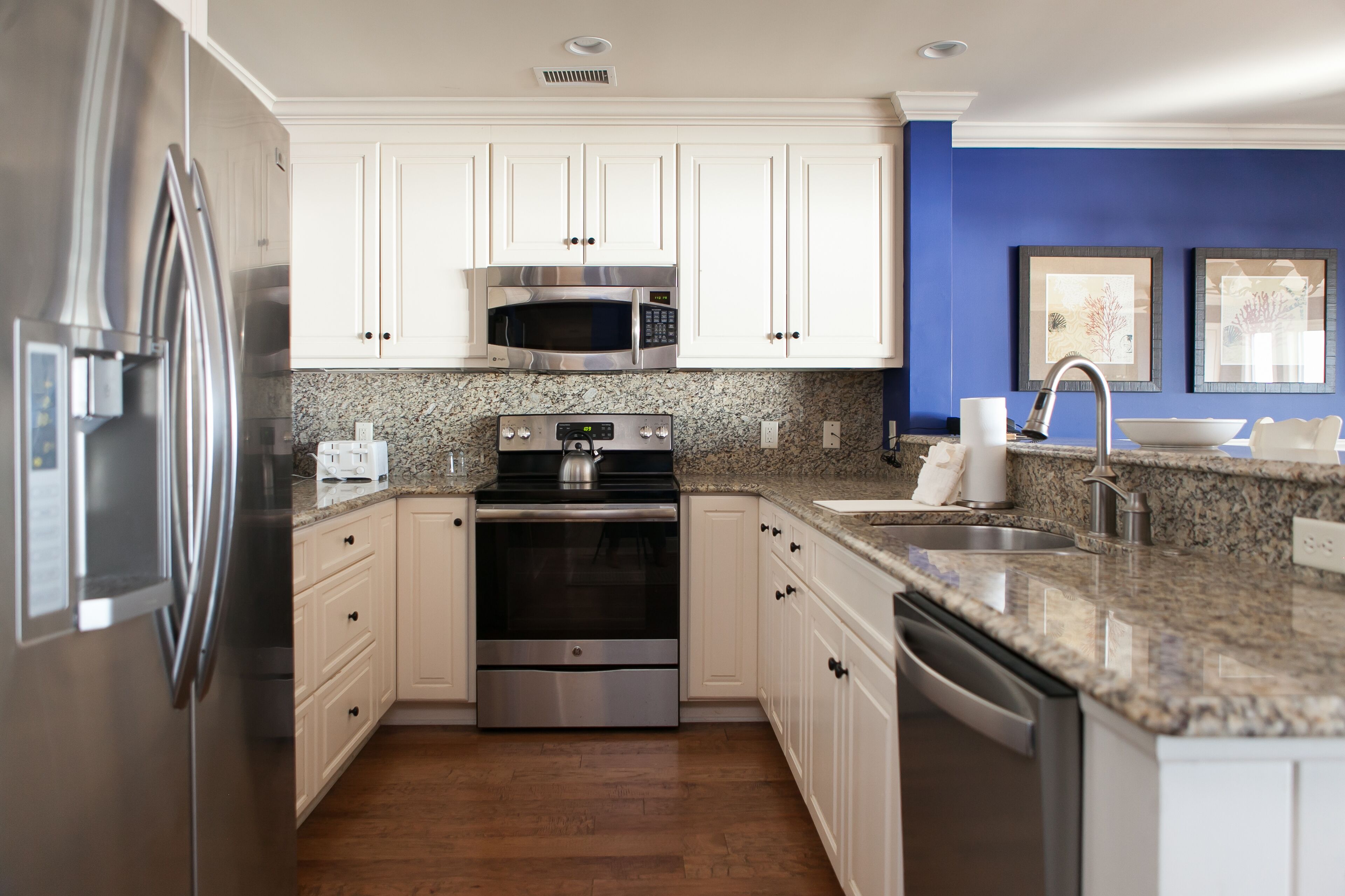 A modern kitchen with white cabinets, stainless steel appliances, granite countertops, and a blue accent wall.
