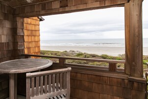 Um deck de madeira com mesa e banco, com vista para uma praia, oceano e vegetação.