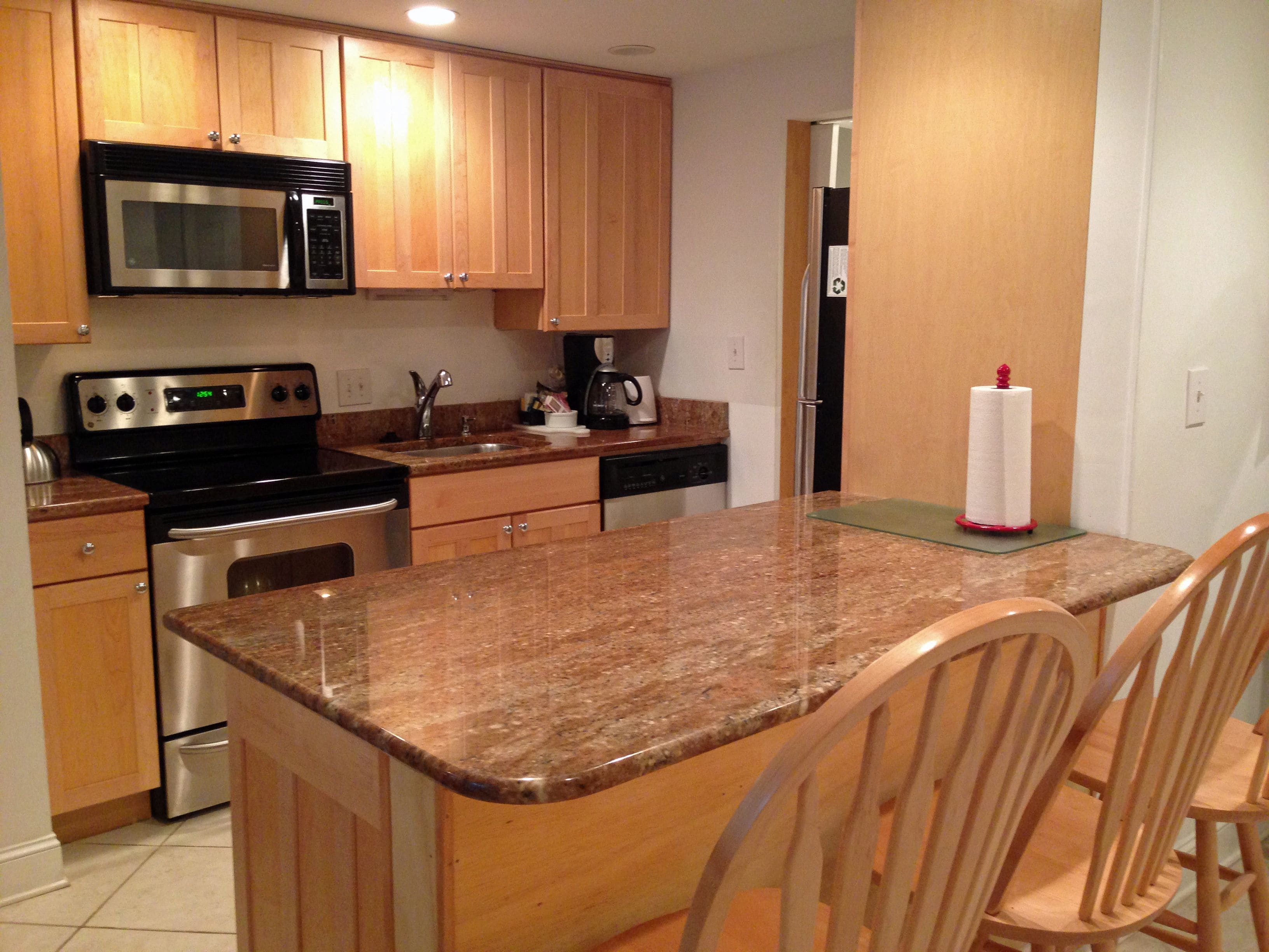 Una cocina con armarios de madera, electrodomésticos de acero inoxidable, encimeras de granito y una isla central con sillas.