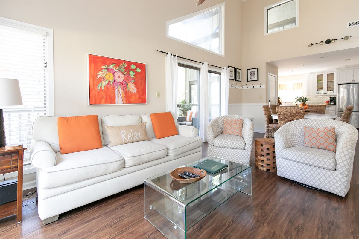 Un salon spacieux avec un canapé blanc, deux fauteuils, une table basse en verre et une grande fenêtre.