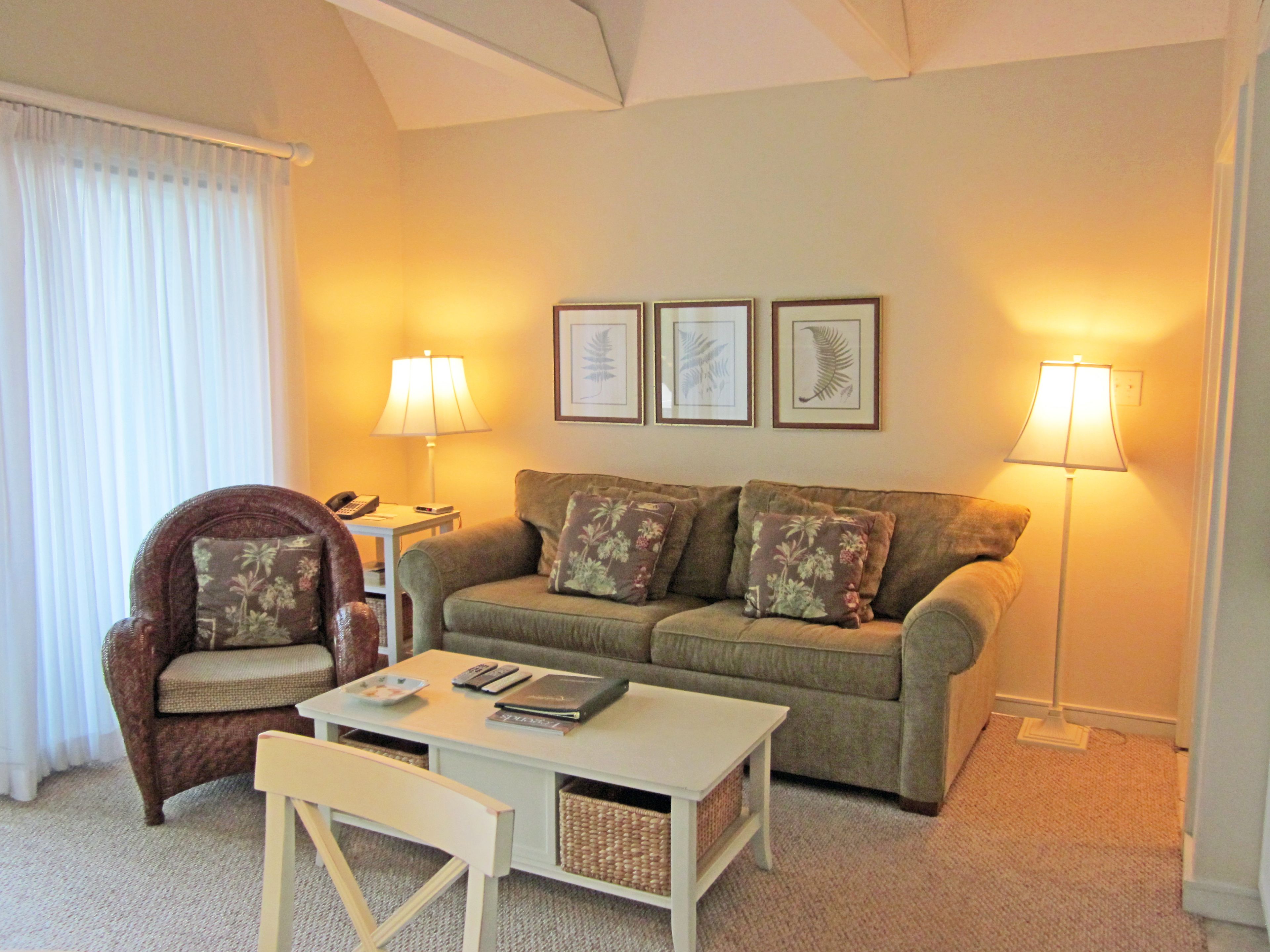 A living room with a sofa, armchair, coffee table, and two lamps. There are framed pictures on the wall and a telephone on the armchair.