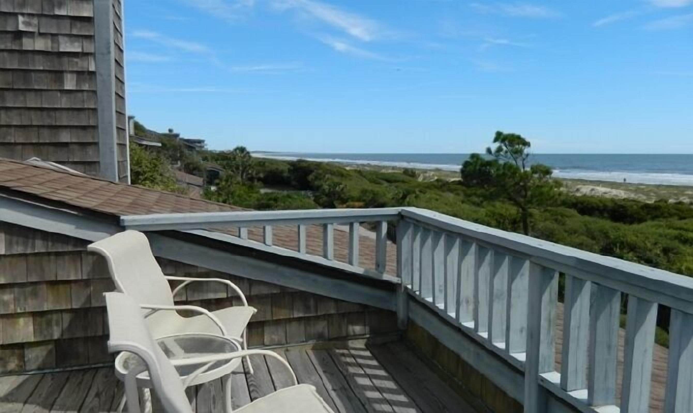 Eine Holzterrasse mit weißen Stühlen mit Blick auf einen Strand.