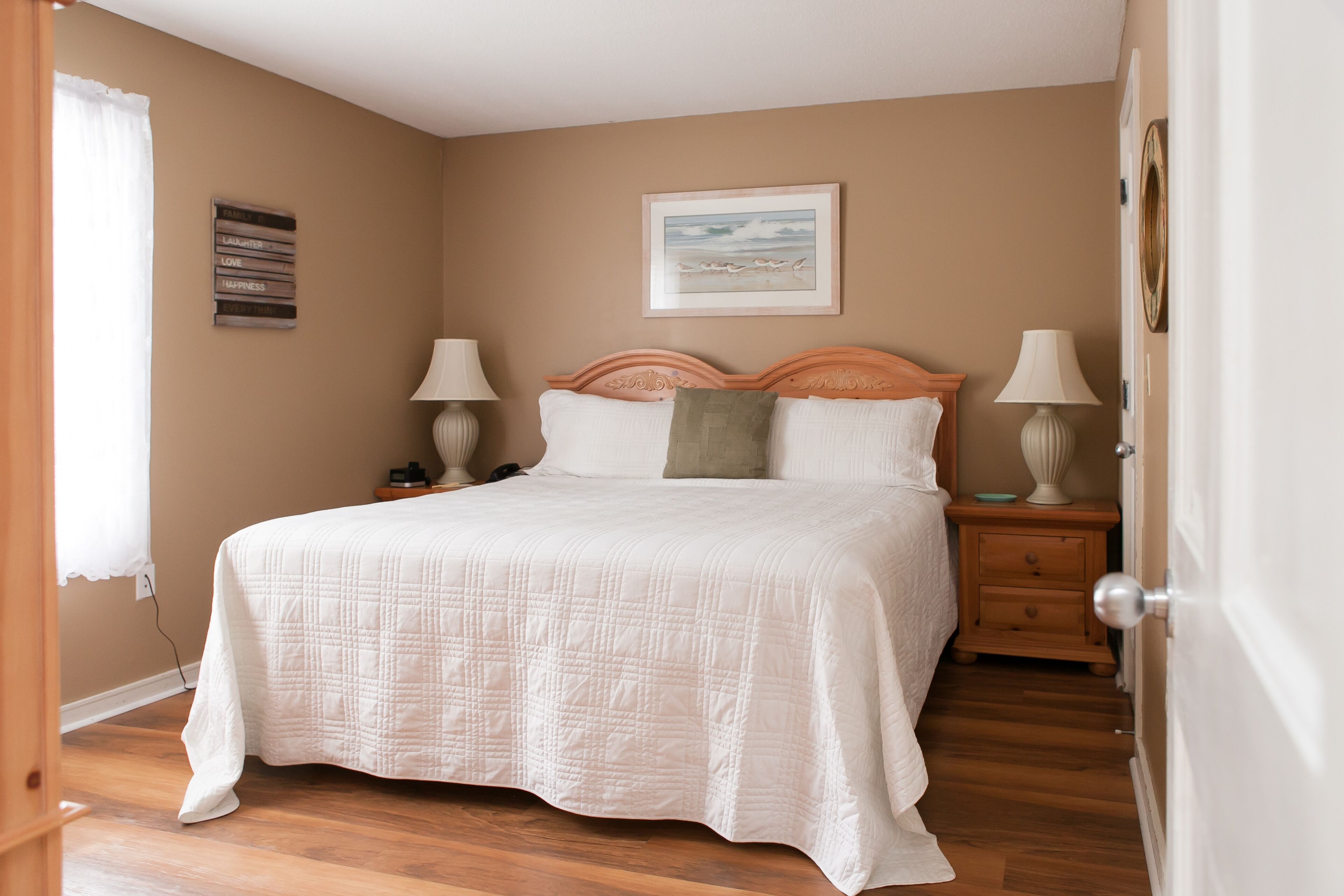 A bedroom with a queen-sized bed, two bedside tables with lamps, a framed picture on the wall, and a wooden floor.