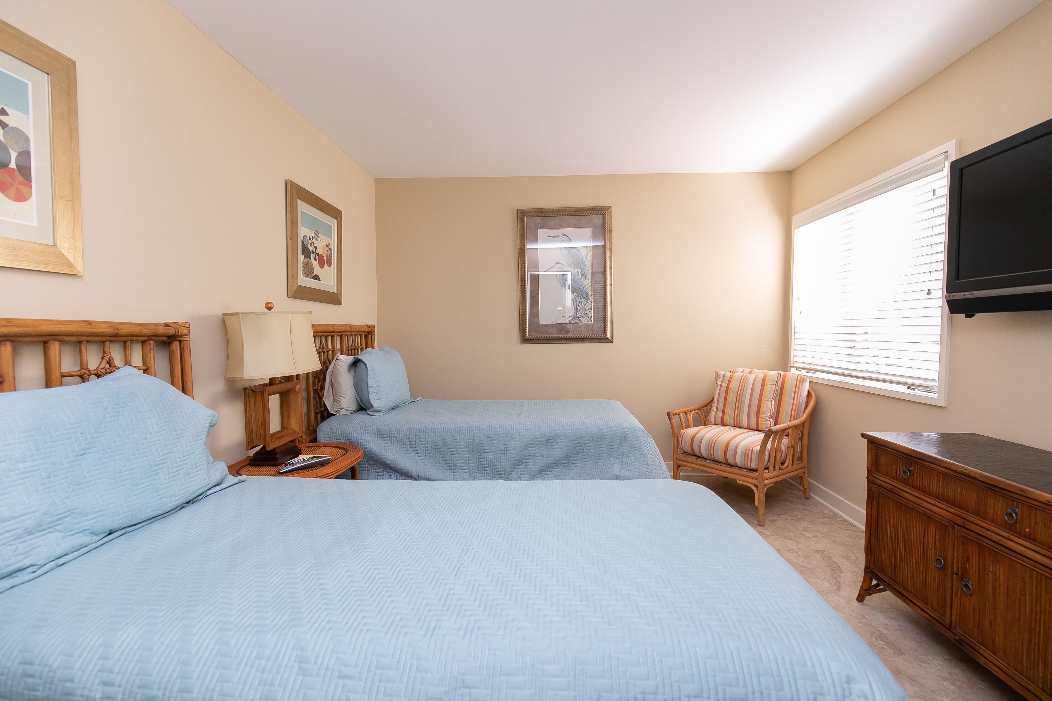 A bedroom with two beds, a chair, a dresser, and a TV.