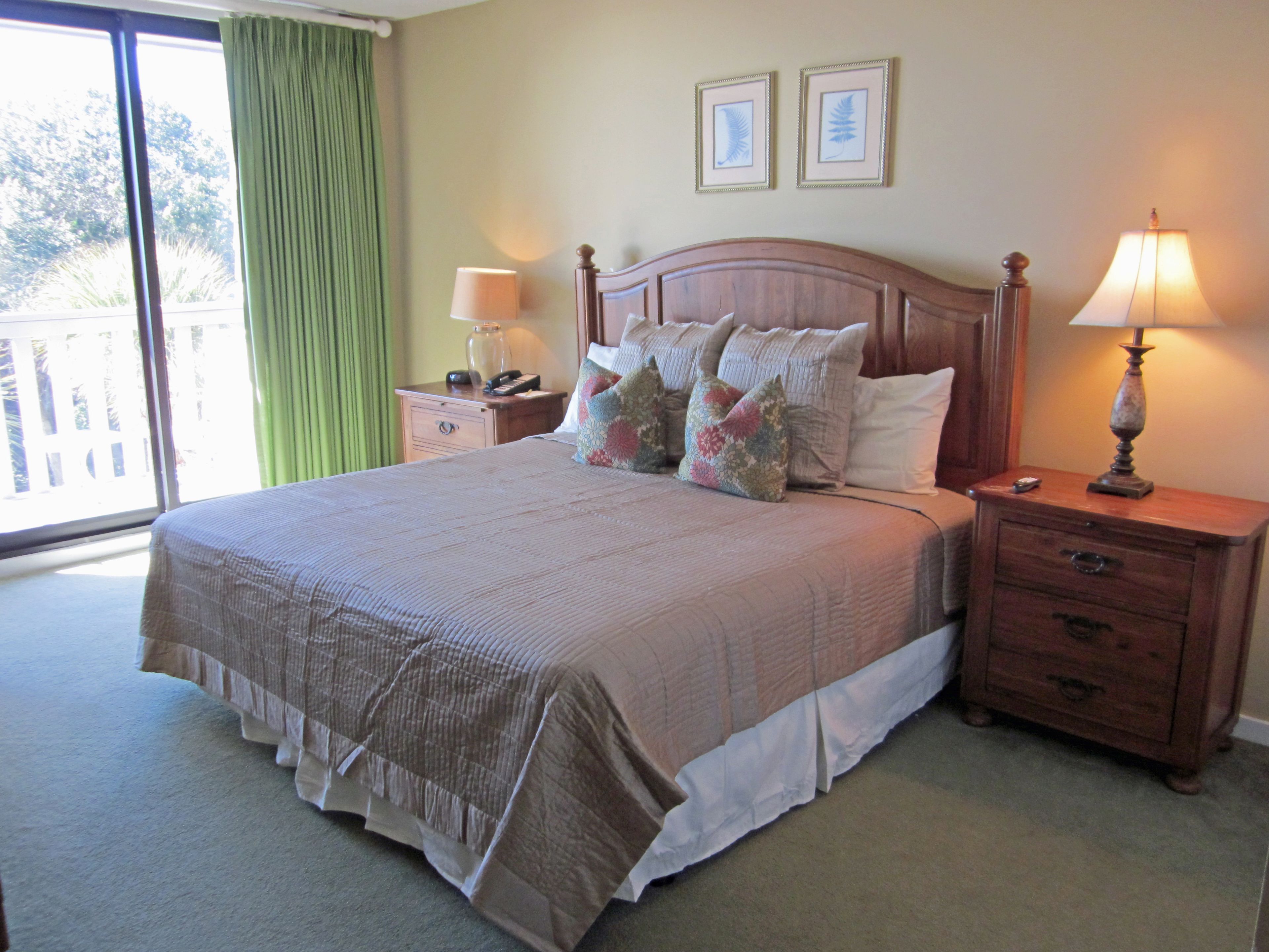 A neatly made bed with a wooden headboard, two bedside tables with lamps, and a view of the outdoors through a large window.