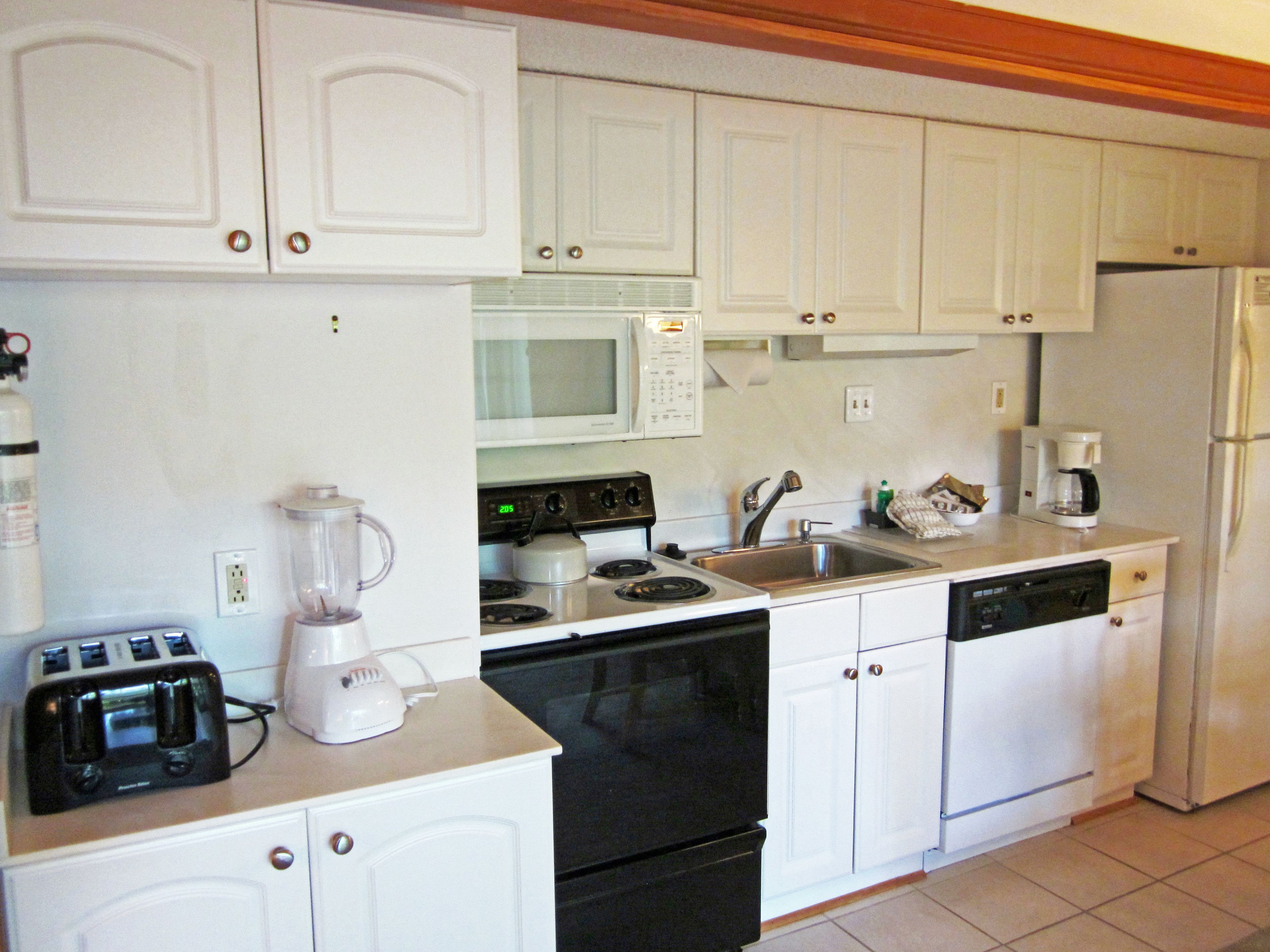 Een compacte keuken met witte kastjes, een magnetron, fornuis, oven, vaatwasser en een koffiezetapparaat.
