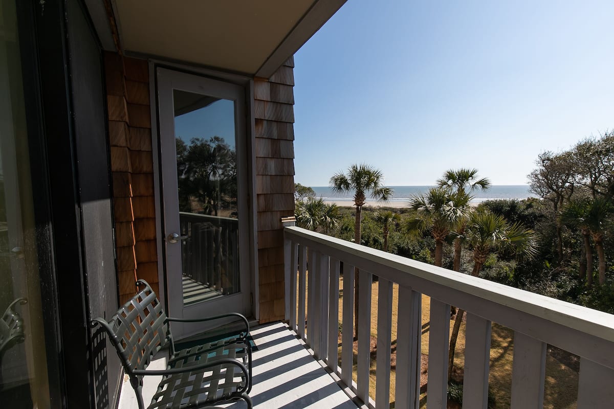 Un balcon donnant sur la plage, un banc et une porte menant à l’intérieur.