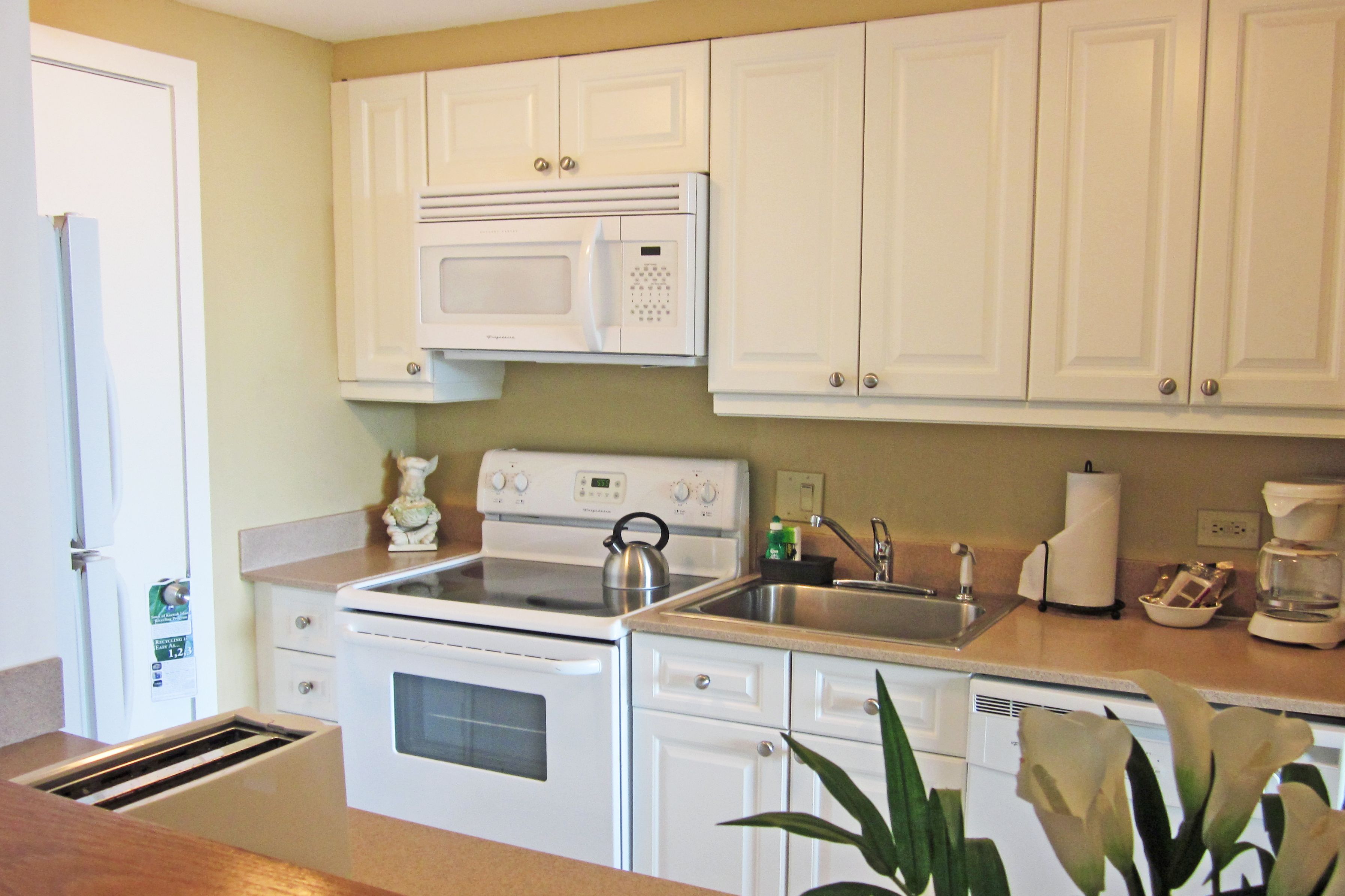 A kitchen with white cabinets, a microwave, a stove, a sink, and a coffee maker.