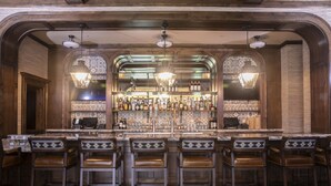 Een bar met een lange toonbank, verschillende krukken en een ruim assortiment flessen en glazen.
