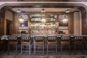 Uma área de bar com um balcão comprido, vários bancos e uma variedade de garrafas e copos.