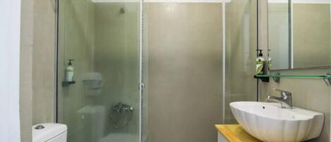 Un baño moderno con ducha envuelta en vidrio, un lavabo blanco y una encimera de madera.