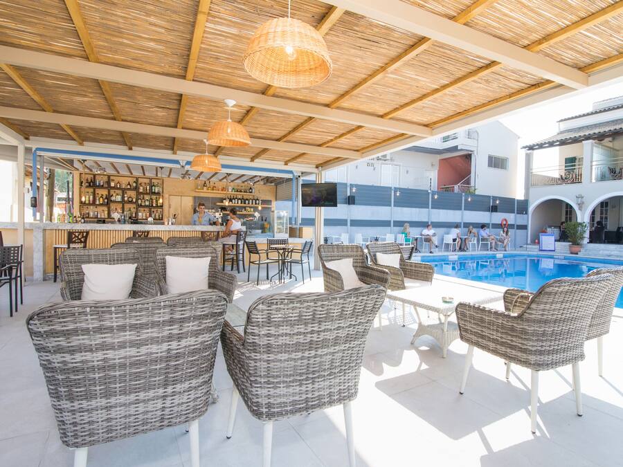 Un área de bar al aire libre con mobiliario de mimbre, una piscina y una barra llena de botellas variadas.